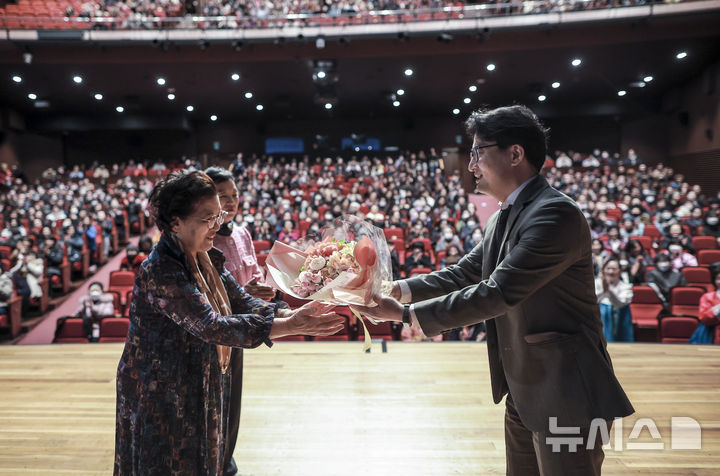 [서울=뉴시스] 정병혁 기자 = 4일 서울 마포구 마포아트센터에서 열린 2025학년도 일성여자중고등학교 입학식에서 최고령 입학생인 정숙자 씨가 교무부장으로 부터 꽃다발을 전달받고 있다. 2025.03.04. jhope@newsis.com
