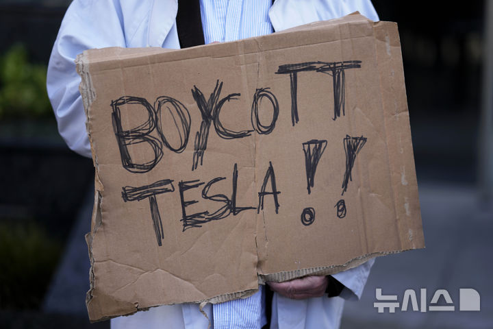 [리스본=AP/뉴시스] 지난 9일(현지 시간) 포르투갈 리스본에 있는 테슬라 전시관 앞에서 한 참가자가 손팻말을 들고 반테슬라 시위에 참여하고 있다. 2025.03.11.