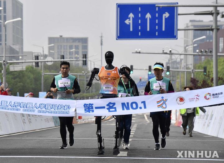 [베이징=신화/뉴시스] 19일 중국 베이징 이좡 경제기술개발구에서 열린 휴머노이드 로봇 하프마라톤에서 우승한 로봇 '톈궁 울트라'가 참가팀 인원들과 함께 달리고 있다. 2025.04.23.