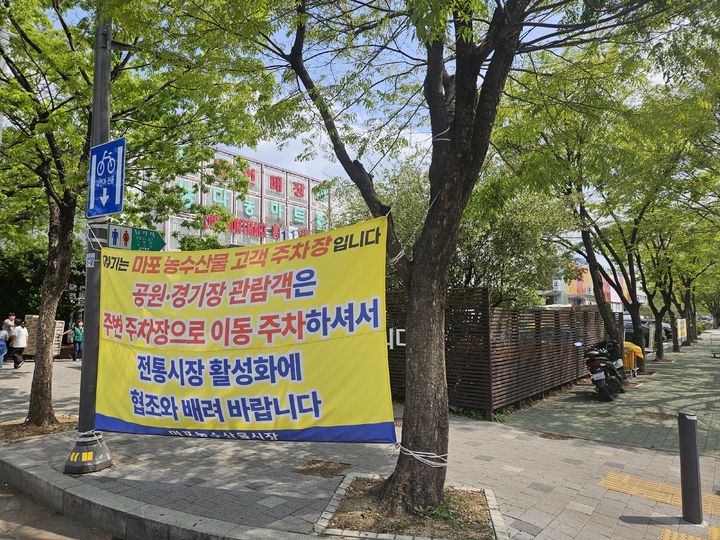 [서울=뉴시스] 이태성 기자 = 21일 오후 서울 마포농수산물시장 주차장 입구에 '공원·경기장 관람객은 이동 주차해달라'는 내용의 현수막이 걸려있다. 2025.04.21. victory@newsis.com *재판매 및 DB 금지