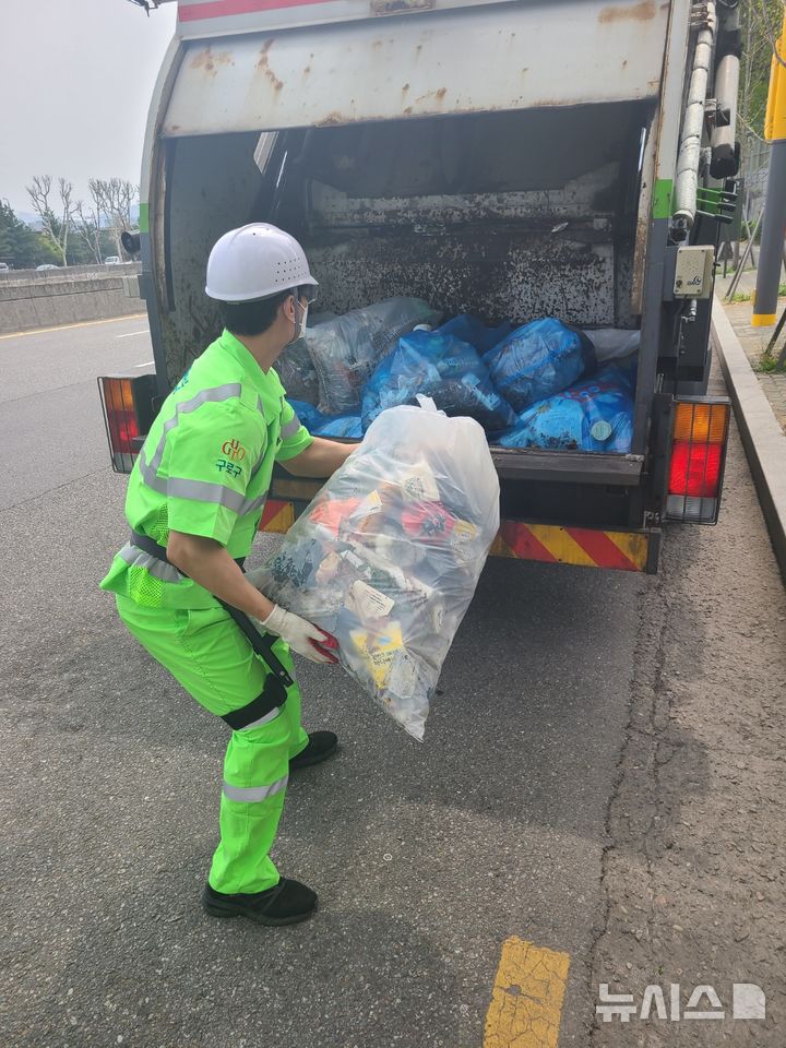 [서울=뉴시스]구로구 환경미화원이 근력증강 착용형(웨어러블)로봇을 착용하고 쓰레기봉투를 청소차로 옮기고 있다.