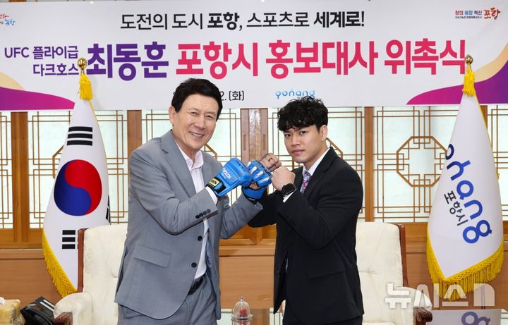 [포항=뉴시스] 송종욱 기자 = 포항시가 세계적인 종합 격투기 무대 UFC 플라이급 최동훈 선수를 홍보대사로 위촉했다. 사진은 홍보대사 위촉식 후 이강덕(왼쪽) 시장이 파이트 글로버를 끼고 최 선수와 기념 촬영하는 모습. (사진=포항시 제공) 2025.04.22. photo@newsis.com 