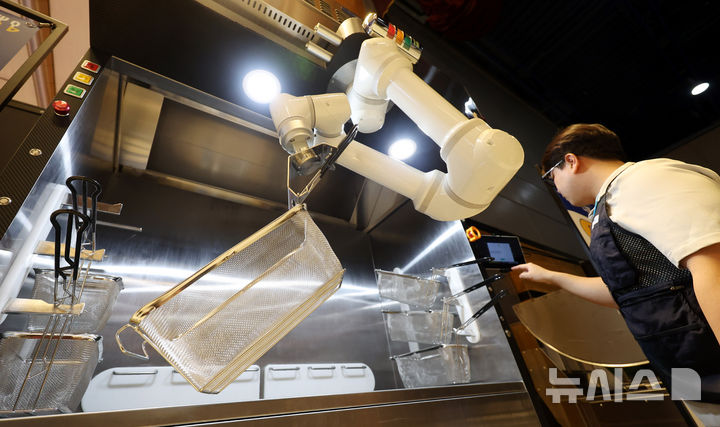 [서울=뉴시스] 추상철 기자 = 사진은 지난 4월 29일 오전 서울 강남구 코엑스에서 열린 '2025 우수급식외식산업전'에서 참가업체 관계자가 로봇팔을 활용한 튀김기 공기정화형 환기시스템 시연을 하고 있는 모습. 2025.04.29. scchoo@newsis.com