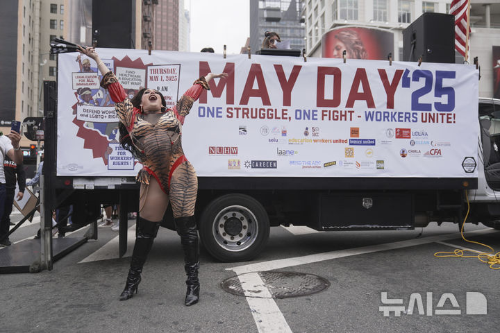 [로스앤젤레스=AP/뉴시스] 1일(현지 시간) 미 캘리포니아주 로스앤젤레스에서 열린 노동절 시위 중 한 여성이 노동절 현수막 앞에서 퍼포먼스를 펼치고 있다. 2025.05.02.