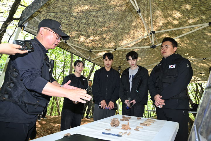 [서울=뉴시스] 발굴팀장(나군 최인건, 좌측)에게 현장에서 발굴된 유품에 대해 설명을 듣고 있는 최태성 역사 커뮤니케이터와 국방부·국가보훈부 2030 자문단. (사진=국방부 제공) 2025.05.02. photo@newsis.com *재판매 및 DB 금지