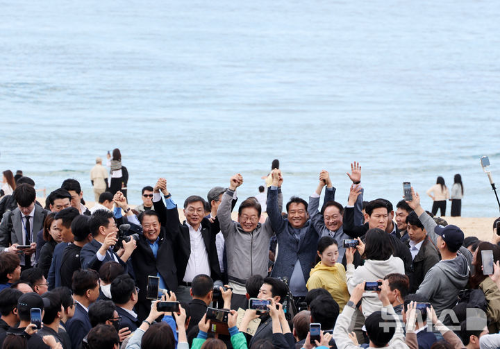 [강릉=뉴시스] 조성우 기자 = 민심을 청취하는 '경청 투어'에 나선 이재명 더불어민주당 대선후보가 3일 강원도 강릉시 안목해변 카페거리에서 이병주 의원, 이 후보 직속 이광재 국가미래정책위원회 공동위원장 등과 손을 맞잡고 주민들과 관광객들에게 인사하고 있다. 2025.05.03. xconfind@newsis.com