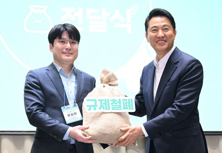 [서울=뉴시스] 오세훈 서울시장이 7일 열링 '규제철폐 100일 성과보고회'에서 시민 제안이 담긴 규제철폐 모래주머니를 전달받고 있다. 2025.05.07 (사진 제공=서울시) photo@newsis.com *재판매 및 DB 금지