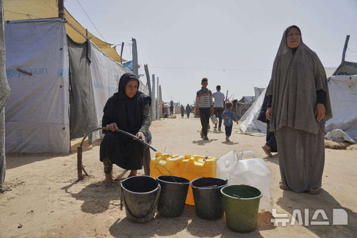 [칸유니스=AP/뉴시스] 지난 11일(현지 시간) 가자지구 칸유니스 천막촌에서 팔레스타인 난민들이 파이프에서 나오는 물을 받고 있다. 2025.05.15.