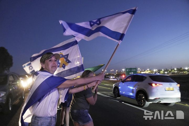 [레임=AP/뉴시스] 12일(현지 시간) 팔레스타인 무장 정파 하마스가 석방한 미국·이스라엘 이중국적 병사 에단 알렉산더가 탑승한 차량이 이스라엘 남부 레임의 군 기지에 도착하자, 미 뉴저지주 출신의 한 여성이 이스라엘 국기를 흔들며 그를 환영하고 있다. 알렉산더는 뉴저지 출신으로, 가자지구에 억류돼 있던 마지막 미국인 생존자로 알려졌다. 2025.05.13.