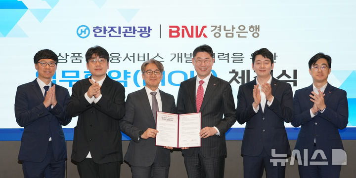 [창원=뉴시스]BNK경남은행 이주형(오른쪽서 세 번째) 부행장과 ㈜한진관광 이장훈 대표이사가 상품·금융서비스 개발 협력을 위한 전략적 업무협약을 체결하고 있다.(사진=BNK경남은행 제공) 2025.05.14. photo@newsis.com