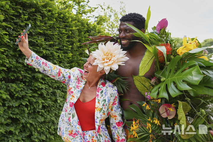 [런던=AP/뉴시스] 19일(현지 시간) 영국 런던 첼시병원에서 열린 2025 첼시 플라워쇼 사전행사에서 한 관람객이 꽃으로 만든 의상을 입은 모델과 기념촬영 하고 있다. 2025.05.20.