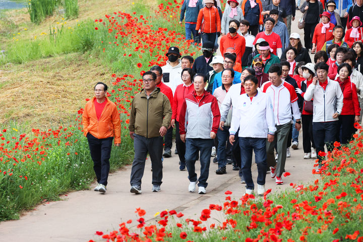 [괴산=뉴시스] 24일 '2025 빨간맛페스티벌'의 대표 프로그램 '빨간꽃길 괴산 걷기대회'가 열린 충북 괴산군 동진천변에서 참가자들이 붉게 물든 양귀비 꽃길을 따라 봄 정취를 만끽하고 있다. (사진=괴산군 제공) 2025.05.24. photo@newsis.com&nbsp; *재판매 및 DB 금지