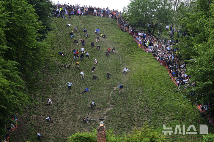 [브록워스=AP/뉴시스] 26일(현지 시간) 영국 글로스터셔주 브록워스의 쿠퍼스 힐에서 연례 치즈 굴리기 대회가 열려 남자부 참가자들이 언덕을 굴러 내려오고 있다. 이 대회는 약 180m 거리의 가파른 언덕에서 구르는 치즈를 잡아 결승선에 먼저 들어오는 사람이 우승하는 경기이다. 2025.05.27.