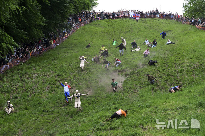 [브록워스=AP/뉴시스] 26일(현지 시간) 영국 글로스터셔주 브록워스의 쿠퍼스 힐에서 연례  치즈 굴리기 대회가 열려 남자부 참가자들이 언덕을 굴러 내려오고 있다. 이 대회는 약 180m 거리의 가파른 언덕에서 구르는 치즈를 잡아 결승선에 먼저 들어오는 사람이 우승하는 경기이다. 2025.05.27.