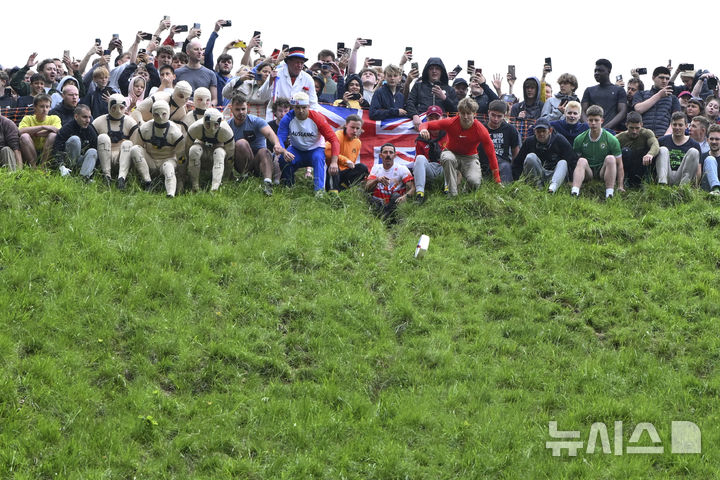 [브록워스=AP/뉴시스] 26일(현지 시간) 영국 글로스터셔주 브록워스의 쿠퍼스 힐에서 연례  치즈 굴리기 대회가 열려 남자부 참가자들이 언덕을 굴러 내려오고 있다. 이 대회는 약 180m 거리의 가파른 언덕에서 구르는 치즈를 잡아 결승선에 먼저 들어오는 사람이 우승하는 경기이다. 2025.05.27.