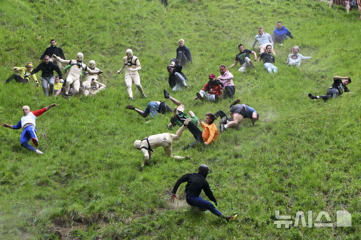 [브록워스=AP/뉴시스] 26일(현지 시간) 영국 글로스터셔주 브록워스의 쿠퍼스 힐에서 연례  치즈 굴리기 대회가 열려 남자부 참가자들이 언덕을 굴러 내려오고 있다. 이 대회는 약 180m 거리의 가파른 언덕에서 구르는 치즈를 잡아 결승선에 먼저 들어오는 사람이 우승하는 경기이다. 2025.05.27.