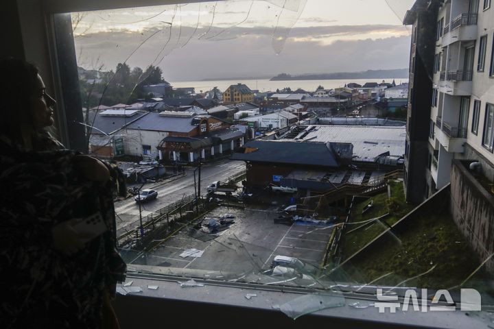 [ 푸에르토 바라스( 칠레)= AP/뉴시스]칠레의 푸에르토 바라스 시내에서 26일(현지시간) 토네이도로 인해 깨어진 유리창을 통해 피해지역을 내다보고 있는 한 여성 주민. 2025.05. 27. 