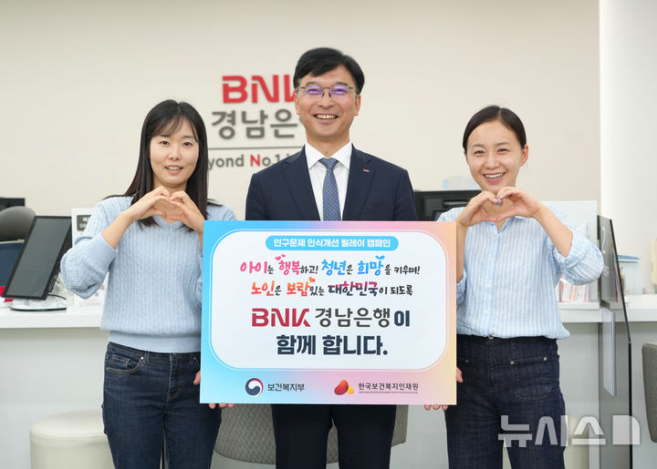 [창원=뉴시스]BNK경남은행 임재문(가운데) 상무가 자녀가 있는 직원 2명과 함께 '인구문제 인식 개선 릴레이 캠페인' 동참 퍼포먼스를 하고 있다.(사진=BNK경남은행 제공)2025.05.27. photo@newsis.com