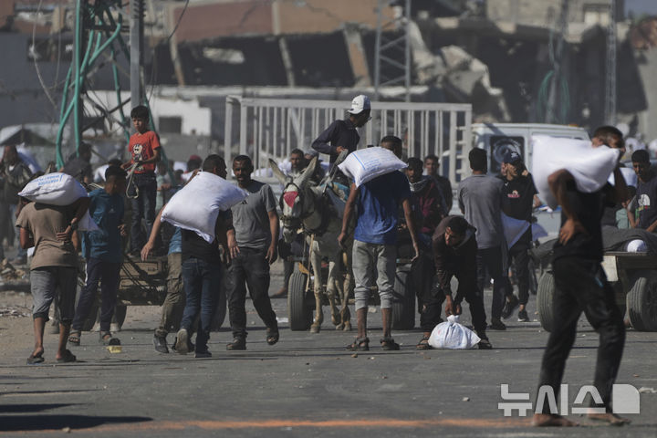 [자와이다=AP/뉴시스] 28일(현지 시간) 가자지구 중부 자와이다에서 유엔 세계식량계획(WFP) 창고를 습격한 팔레스타인 주민들이 밀가루 자루를 들고 돌아가고 있다. 2025.05.29.