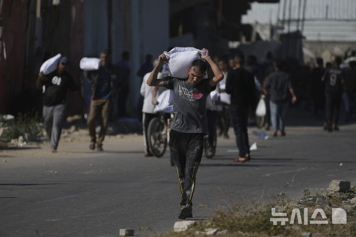 [가자지구=AP/뉴시스] 28일(현지 시간) 가자지구 자와이다에 위치한 유엔 세계식량계획 창고를 습격한 팔레스타인인들이 밀가루를 들고 이동하고 있다. 2025.05.29.