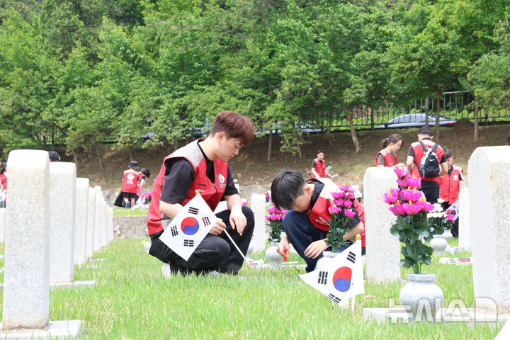 [서울=뉴시스] 롯데건설 '샤롯데 봉사단'이 묘비 옆에 태극기를 꽂고 있다. (사진=롯데건설 제공)