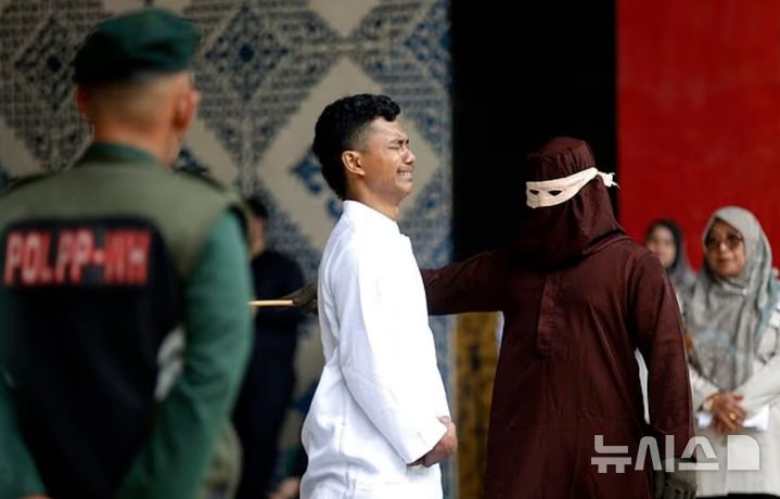 [뉴시스] 인도네시아에서 혼외 성관계를 한 혐의를 받는 남성이 군중이 지켜보는 앞에서 경찰에게 채찍질을 당하고 있는 모습이다. (사진=데일리메일) 2025.6.5 