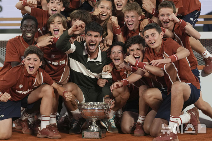 [파리=AP/뉴시스] 카를로스 알카라스(2위·스페인)가 8일(현지 시간) 프랑스 파리 롤랑가로스에서 열린 프랑스오픈 남자 단식 정상에 올라 트로피를 들고 볼키즈와 함께 기념 촬영하고 있다. 알카라스는 결승전에서 얀니크 신네르(1위·이탈리아)와 5시간 29분 대접전 끝에 3-2(4-6 6-7 6-4 7-6 7-6) 역전승을 거두고 대회 2연패를 달성했다. 2025.06.09.