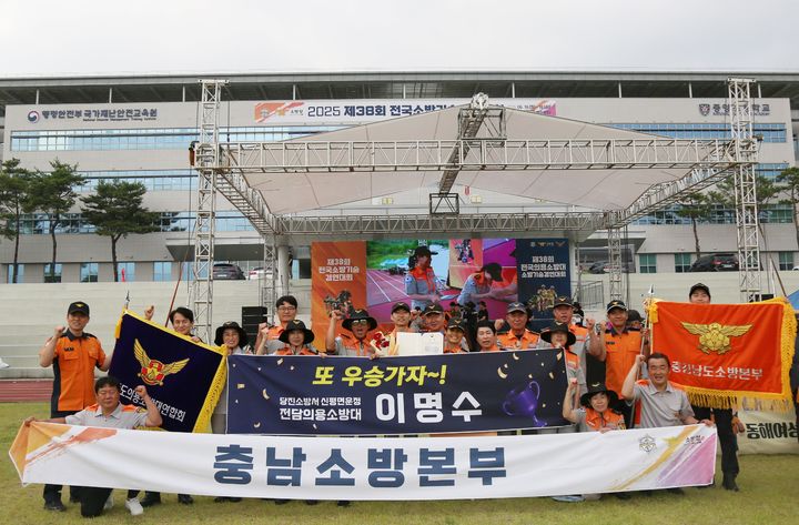 [당진=뉴시스] 이명수 당진소방서 의용소방대원이 지난 16일 공주 중앙소방학교에서 열린 '2025년 전국소방기술경연대회' 호스전개 부문에서 1위를 차지한 뒤 대회장에서 관계자들과 기념 사진을 찍고 있다. (사진=당진소방서 제공)2025.06.17. photo@newsis.com *재판매 및 DB 금지