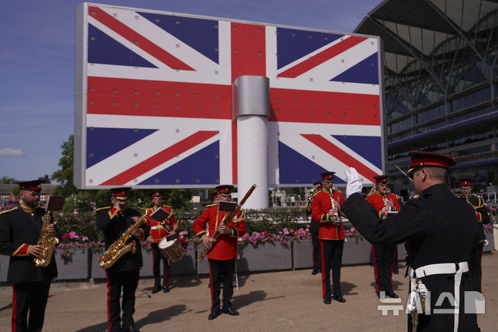 [애스콧( 영국)=AP/뉴시스] 2025년6월 18일 영국 애스콧 왕립 경마대회장에서 거대한 전광판 국기 앞에서 연주하는 군악대. 영국왕실은 왕실 비용을 절감하고 국가적 현대화에 부응하기 위해 왕실전용 열차 운행을 폐지하기로 했다고 6월 30일 발표했다. 2025. 07.01. 