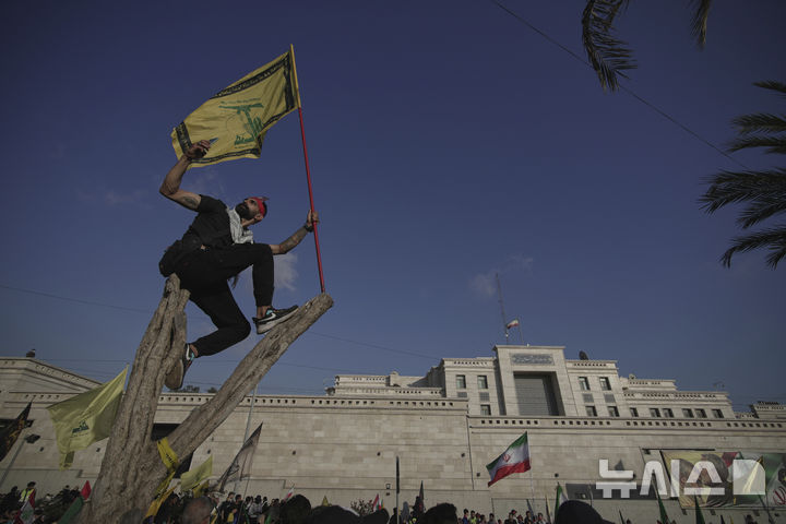 [베이루트=AP/뉴시스] 지난 6월 25일(현지 시간) 레바논 베이루트 주재 이란 대사관 밖에서 열린 이란 지지 집회 도중, 한 헤즈볼라 지지자가 나무 위에 올라 헤즈볼라 깃발을 흔들며 셀카를 찍고 있다. 집회 주최 측은 "미국과 이스라엘의 침략을 무너뜨린" 이란을 기리고 지지하기 위해 집회를 열었다고 밝혔다. 2025.11.09.