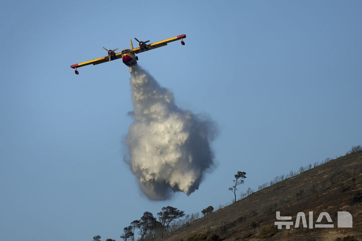 [티마리=AP/뉴시스] 그리스 폭염으로 기온이 40도에 육박한 26일(현지 시간) 아테네 남쪽 티마리에서 소방 항공기 한 대가 산불 진압을 위해 물을 뿌리고 있다. 현지 당국은 인근 지역 5곳에 대해 대피령을 내렸다. 2025.06.29.