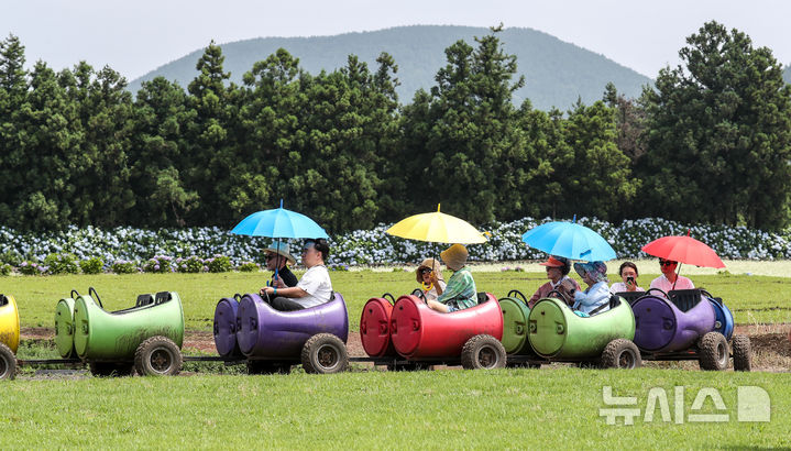 [서귀포=뉴시스] 우장호 기자 = 장마가 소강상태에 놓인 27일 오전 제주 서귀포시 표선면 보롬왓 농장에서 우산을 쓴 방문객들이 깡통열차를 타며 즐거운 한때를 보내고 있다. 2025.06.27. woo1223@newsis.com