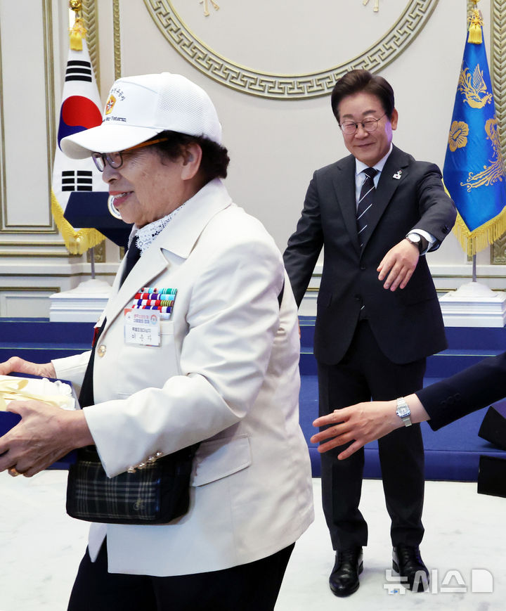 [서울=뉴시스] 최진석 기자 = 이재명 대통령이 27일 청와대 영빈관에서 열린 '호국보훈의 달, 대통령의 초대' 행사에서 광목이불 선물을 받은 특별초청 대상자인 6·25전쟁 참전유공자 이춘자 참전용사가 들어가려 하자 기념촬영을 요청하며 손짓하고 있다. (대통령실통신사진기자단) 2025.06.27. myjs@newsis.com