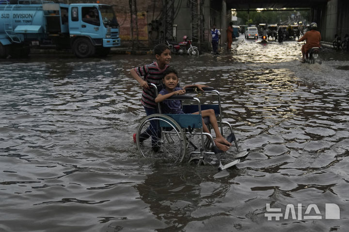 [라호르( 파키스탄)= AP/뉴시스] 계절 폭우로 침수된 파키스탄의 라호르 시내에서 6월 29일 휠체어를 탄 소년과 사촌인 소년이 조심스럽게 길을 건너고 있다. 2025. 06.30. 