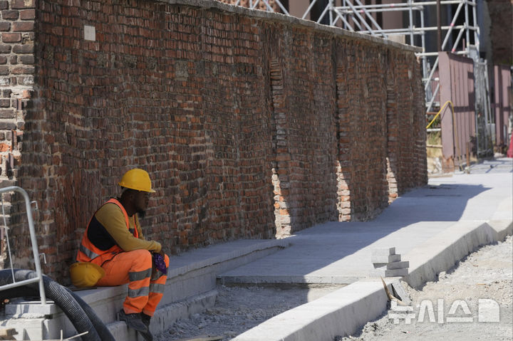[미라노=AP/뉴시스] 2일(현지 시간) 이탈리아 밀라노의 한 도로 공사장에서 한 근로자가 무더위 속 일손을 잠시 멈추고 그늘에 앉아 쉬고 있다. 2025.07.03.