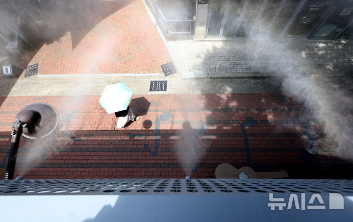 [대구=뉴시스] 이무열 기자 = 폭염이 연일 계속된 4일 대구 중구 김광석다시그리기길에 설치된 쿨링포그(안개형 냉각수) 아래로 한 시민이 양산을 쓰고 이동하고 있다. 2025.07.04. lmy@newsis.com