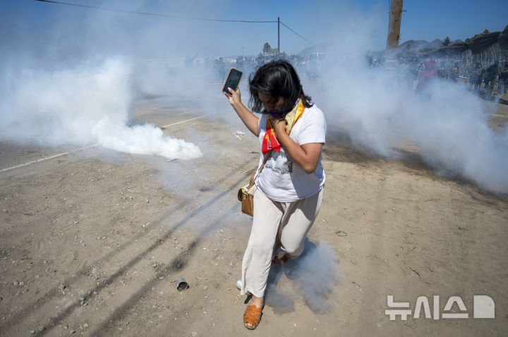 [캐머릴로=AP/뉴시스] 지난달 10일(현지 시간) 미 캘리포니아주 캐머릴로의 '글라스하우스' 대마 농장에서 이민 단속이 벌어진 가운데, 단속 요원들이 차량 진입을 위해 최루탄을 투척하자 한 시위자가 이를 피해 달아나고 있다. 이번 단속에는 이민세관단속국(ICE) 요원들과 군용 차량을 동원한 주 방위군이 동원됐으며, 이에 항의하는 이민자 권리 옹호 활동가들이 현장에서 단속반과 대치했다. 2025.07.11.
