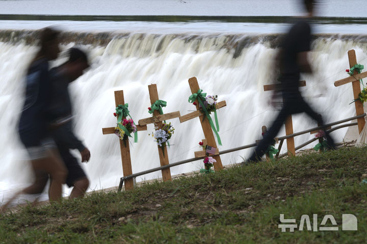[커빌=AP/뉴시스] 13일(현지 시간) 미국 텍사스 커빌에서 대홍수 피해자들을 기리는 임시 추모식에 참석한 사람들이 십자가 옆을 지나가고 있다. 2025.07.14.