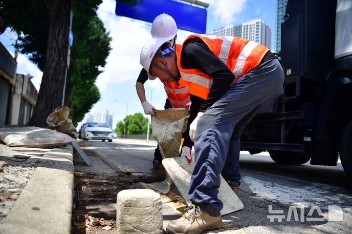 [광주=뉴시스] 이현행 기자=14일 오후 광주 서구 양동 인근에서 서구청 관계자들이 빗물받이를 덮고 있던 나무판자와 10㎏ 남짓한 돌덩이를 치우고 있다. 2025.07.14. lhh@newsis.com