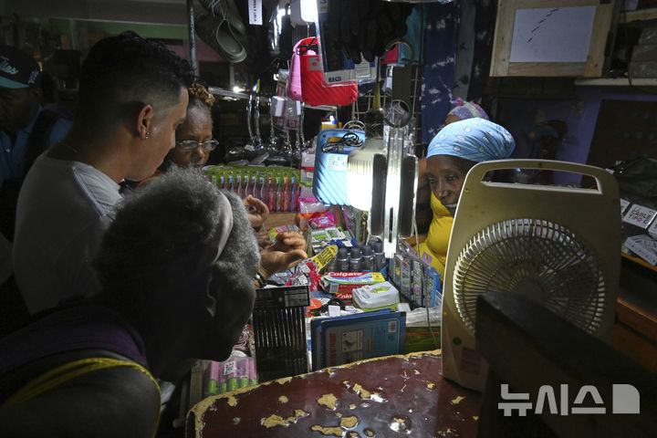 [하바나=AP/뉴시스] 15일(현지 시간) 쿠바 하바나에서 한 상인이 가게에 정전이 발생하자 충전식 램프 조명을 켠 채 고객에게 물건을 판매하고 있다. 2025.07.16.