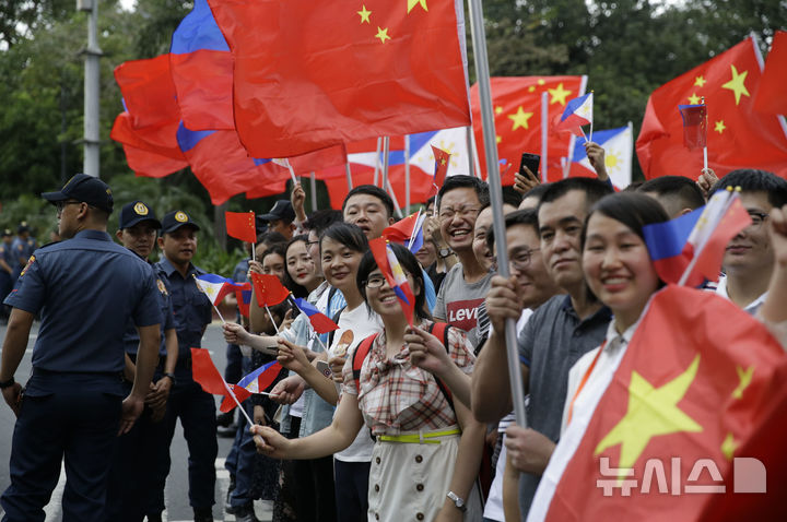[마닐라(필리핀)=AP/뉴시스]2018년 11월20일 필리핀 마닐라의 중국 기업인과 학생들이 필리핀을 방문한 시진핑(習近平) 중국 국가주석이 타고 있는 차량 행렬을 향해 중국 국기를 흔들며 환영하고 있다. 중국 교육부는 18일 필리핀에 있는 중국 유학생들을 대상으로 한 일련의 범죄 발생에 따라 유학생들에게 안전 경고를 발령했다. 2025.07.18.