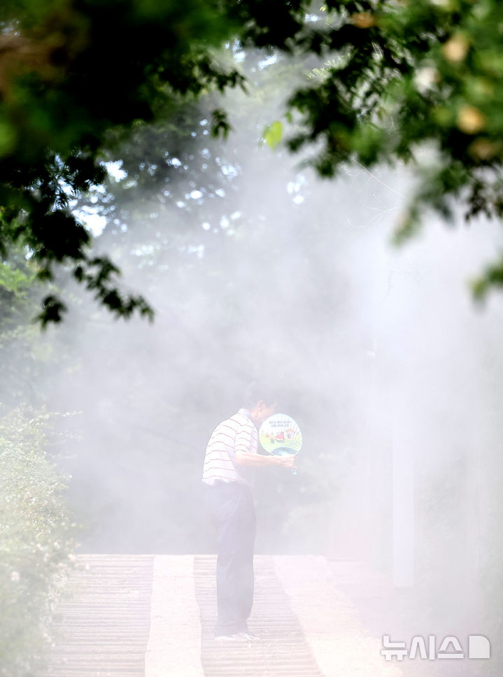 [대구=뉴시스] 이무열 기자 = 폭염이 연일 계속된 23일 대구 중구 청라언덕에 설치된 쿨링포그 아래로 한 시민이 부채를 들고 이동하고 있다. 2025.07.23. lmy@newsis.com