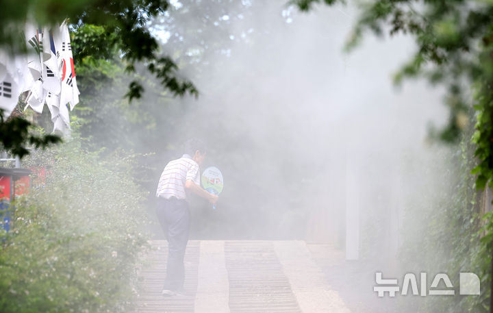 [대구=뉴시스] 이무열 기자 = 폭염이 연일 계속된 23일 대구 중구 청라언덕에 설치된 쿨링포그 아래로 한 시민이 부채를 들고 이동하고 있다. 2025.07.23. lmy@newsis.com