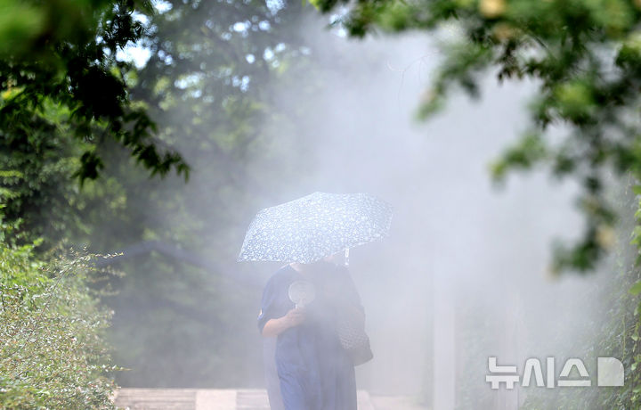 [대구=뉴시스] 이무열 기자 = 폭염이 연일 계속된 23일 대구 중구 청라언덕에 설치된 쿨링포그 아래로 한 시민이 손 선풍기를 들고 이동하고 있다. 2025.07.23. lmy@newsis.com