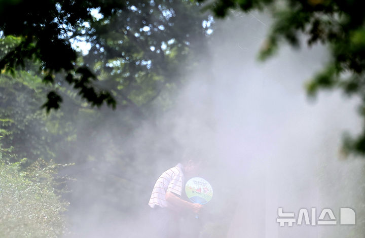 [대구=뉴시스] 이무열 기자 = 폭염이 연일 계속된 23일 대구 중구 청라언덕에 설치된 쿨링포그 아래로 한 시민이 부채를 들고 이동하고 있다. 2025.07.23. lmy@newsis.com