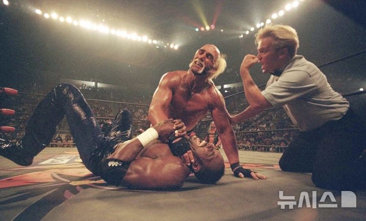 [샌디에이고=AP/뉴시스] 미국 프로레슬링의 전설 '헐크 호건(본명 테리 진 볼레아)'이 24일(현지 시간) 71세를 일기로 별세했다. 사진은 헐크 호건(가운데)이 지난 1998년 열린 PPV 레슬링 경기에서 유타 재즈 농구 스타 칼 말론의 목을 압박하는 모습. 2025.07.25.
