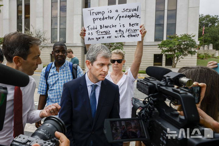 [탤러해시=AP/뉴시스]데이비드 마커스 기슬레인 맥스웰 변호사가 25일(현지시각) 토드 블랑슈 미 법무부장관이 아동 성범죄자 제프리 엡스타인의 조력자인 기슬레인 맥스웰을 장시간 면담한 뒤 기자들에게 상황을 설명하고 있다. 뒤의 시위대가 "트럼프는 성착취자/아동성애자, 토드 블랑슈가 트럼프의 변호사 겸 해결사로 이곳에 와 있다. 그래도 괜찮은가"라고 쓴 팻말을 들고 있다. 2025.7.26. David Oscar Markus, an attorney for Ghislaine Maxwell, talks with the media outside the federal courthouse, Friday, July 25, 2025, in Tallahassee, Fla., after Deputy Attorney General Todd Blanche met with Maxwell, the imprisoned former girlfriend of financier and convicted sex offender Jeffrey Epstein. (AP Photo/Colin Hackley)