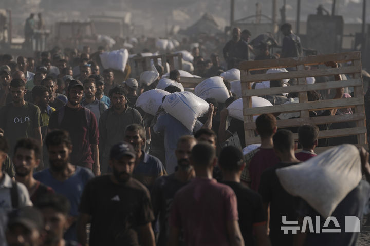 [AP/뉴시스] 26일 가자 북쪽 봉쇄선에서 진입한 구호트럭으로부터 밀가루 포대를 얻은 팔레스타인 주민들이 가자 시티 쪽으로 돌아가고 있다&nbsp; 