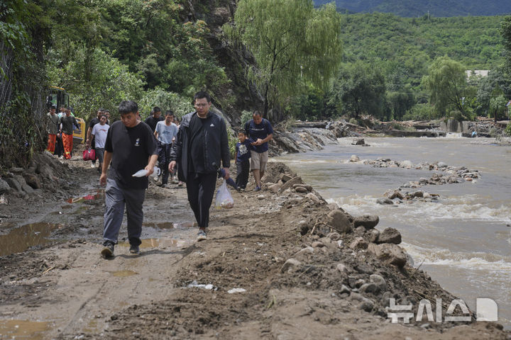 [베이징=AP/뉴시스] 29일(현지 시간) 중국 베이징 교외 미윈구에서 폭우로 홍수 피해를 입은 마을 주민들이 짐을 챙겨 훼손된 도로를 따라 대피하고 있다. 현지 당국은 지난 주말 이후 베이징 전역에 폭우가 쏟아져 미윈구 강수량이 543.4㎜를 기록했고 최소 28명이 숨졌다고 전했다. 2025.07.29.
