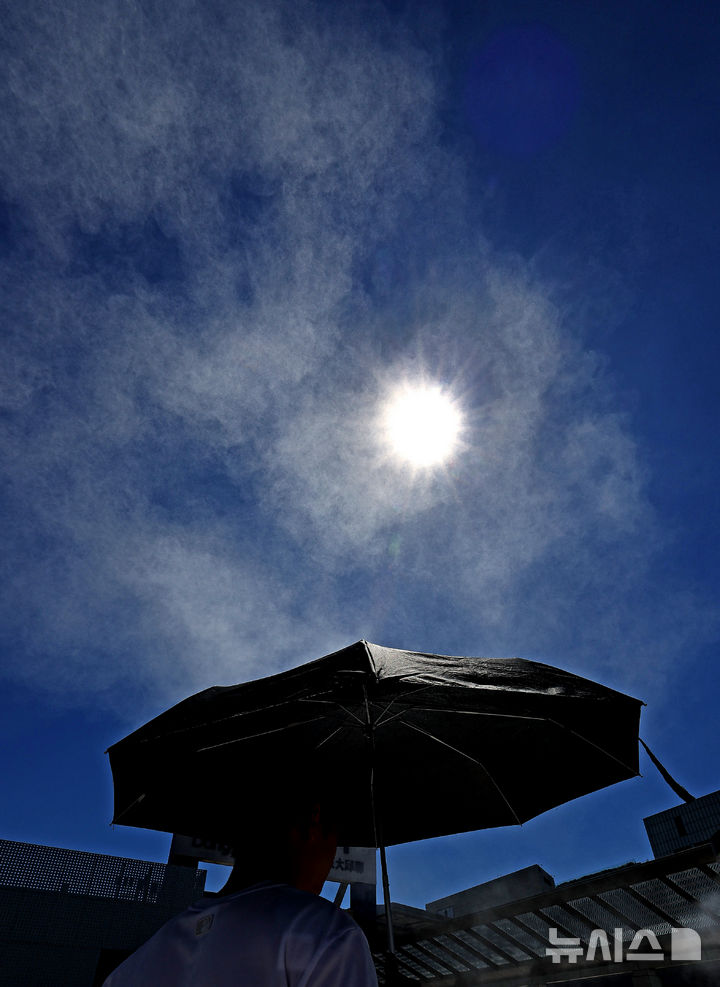 [대구=뉴시스] 이무열 기자 = 폭염이 연일 계속되고 있는 29일 대구 동구 동대구역 광장에 설치된 쿨링포그 아래로 한 시민이 양산을 쓰고 이동하고 있다. 2025.07.29. lmy@newsis.com